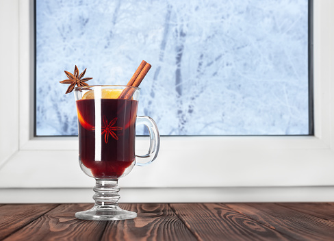 hot mulled wine with cinnamon and anise stars in glass mug on wooden table. Winter alcoholic cocktail. Christmas traditional drink