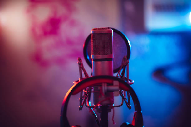 Condenser microphone on boom stand with headphones Condenser microphone on a boom stand, with black headphones in a music studio, vocal booth. rap stock pictures, royalty-free photos & images