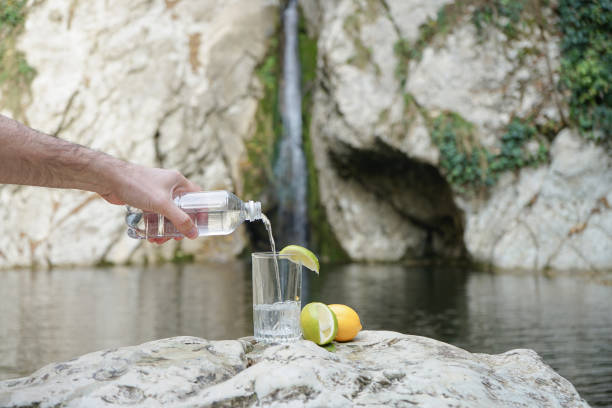 istock Pouring clear drinking water from a biodegradable plastic bottle into a glass which male hand holding in front of a mountain stream 1190825673