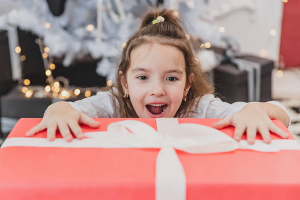 nahaufnahme foto von super aufgeregt junge mädchen eröffnung große weihnachtsgeschenk, während auf wohnzimmer boden sitzen. - praying joy indoors lifestyles stock-fotos und bilder