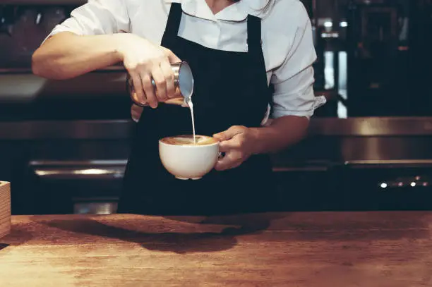 Barista making cappuccino in coffeeshop or cafe, close-up to hands pouring milk