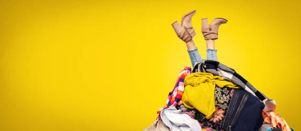 복사 공간이있는 노란색 배경에 옷 더미에서 여성 다리 - 쇼핑광 뉴스 사진 이미지