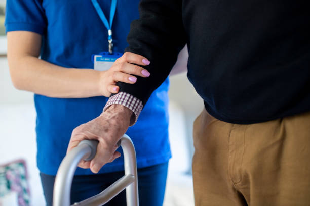 homme aîné avec des mains sur le cadre de marche avec le travailleur de soin - home caregiver senior adult community outreach nursing home photos et images de collection