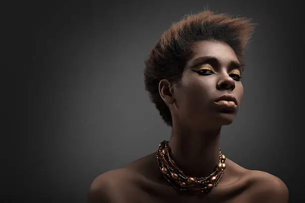 Dark-skinned beautiful fashion model with  professional makeup and hairstyle photographed against gray background .