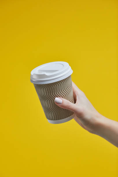 istock Female hand holding a Coffee paper cup on a yellow background 1190837302