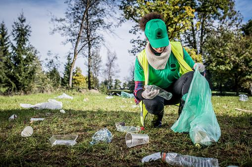 Local cleanup volunteer collecting plastic bottles in public park.