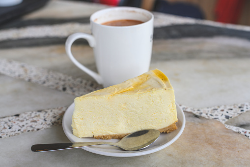 A slice of passion fruit cheesecake and a cup of hot tea on a marble table served at a restaurant at the tea plantation in Cameron Highlands.