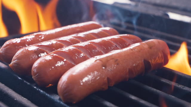 Prepare few sausages and hot dogs On The Hot Flaming BBQ Charcoal Grill. Classic Takeaway Meal. Street food cooked on hot plate. Close up Slow motion
