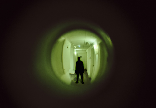 view of a sinister man through the peephole, spy-hole door - concept stalker or criminal mind in general