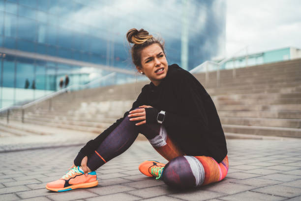 Sportswoman with broken leg sitting on ground,Barcelona Woman with pain in the leg during workout sitting on ground. ankle photos stock pictures, royalty-free photos & images