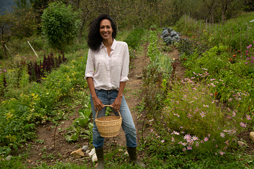 Portrait of smiling young female farm worker holding wicker basket while standing in farm.