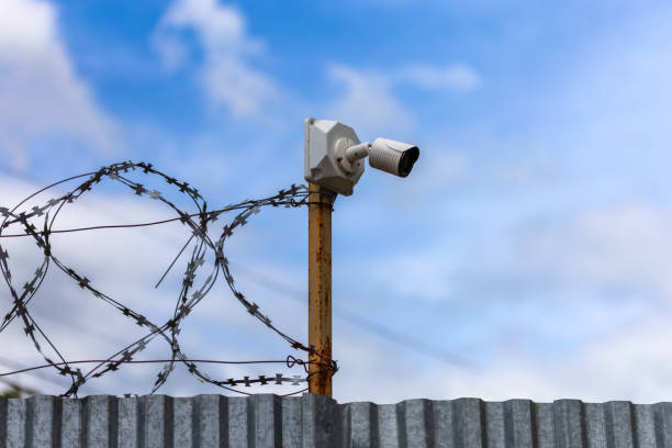 istock Profiled sheet fence with cheap surveillance camera and barbwire with selective focus. 1190856802