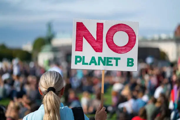 rear view woman at climate change protest fridays for future holding no planet b sign in front of big crowd at demonstration, shallow focus, background blurred