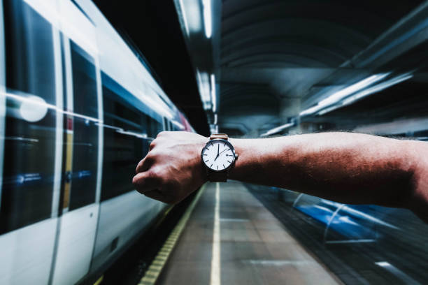Cropped image of a man's hand showing wristwatch on a train station platform while the train is leaving.
