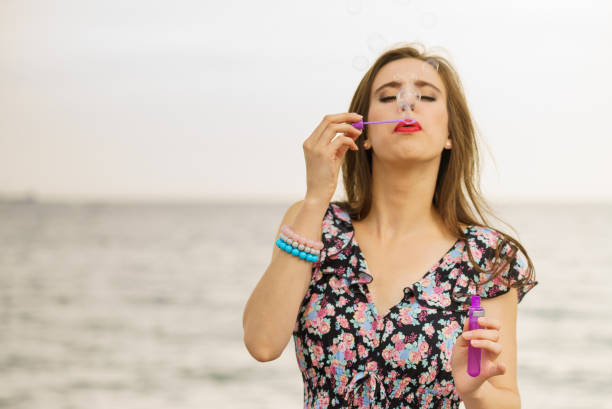 Happiness and carefree concept. Young woman having fun blowing soap bubbles outdoor near sea