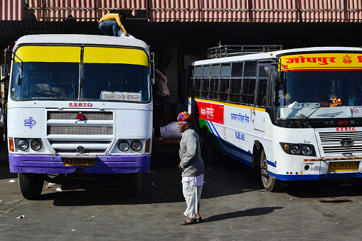 Ajmer, Rajasthan, India - December, 2016: Man in traditional headdress turban and traditional Rajasthan cloth on bus station near two buses. Another man loading bags on the bus roof.