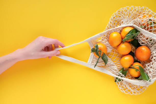 istock A human hand holds a string bag with tangerines on bold yellow color background. 1190876180