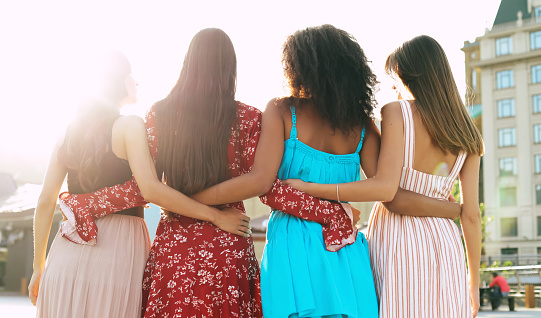 Four attractive women are posing with their backs to the camera, hugging each other by waists and showing their wonderful haircuts.