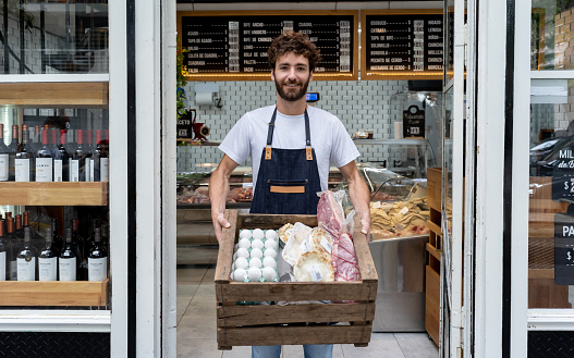 Delivery man at a deli holding a box with products for a customer smiling at camera very happy
