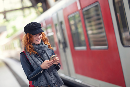A woman standing on a train station platform by a train and checking her phone.