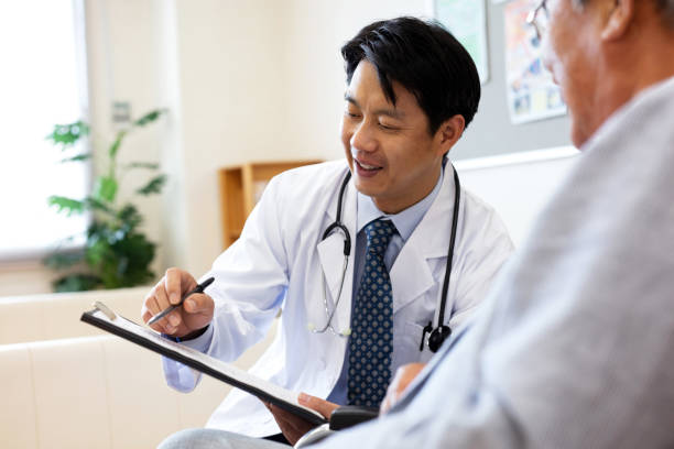 médico masculino sonriente discutiendo sobre el historial médico con el hombre de la tercera edad en el hospital - asian ethnicity doctor patient healthcare and medicine fotografías e imágenes de stock