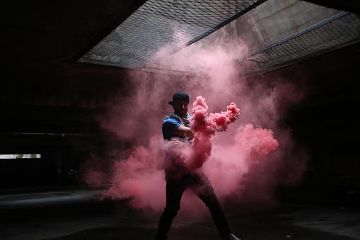 Young man dancing with red smoke in an underground garage. About 25 years old, Caucasian male.