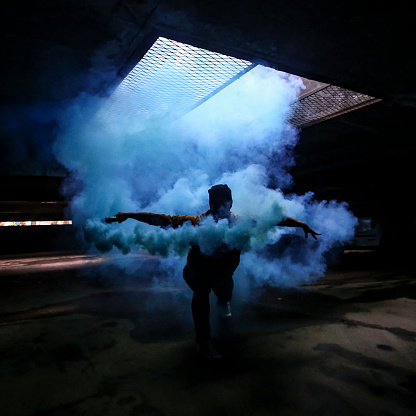 Unrecognizble young man dancing with blue smoke in an underground garage.