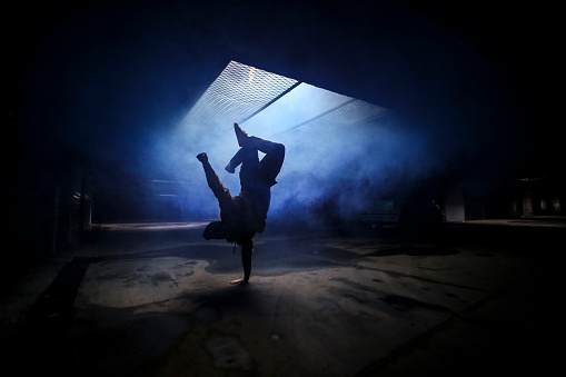 Silhouette of a young unrecognizable man dancing in an underground garage.