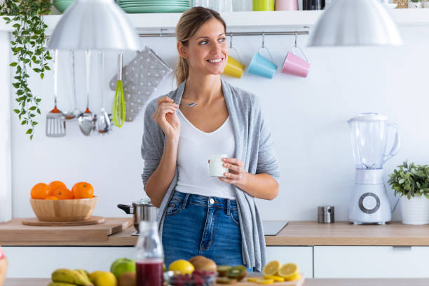 istock Pretty young woman eating yogurt while standing in the kitchen at home. 1190896740