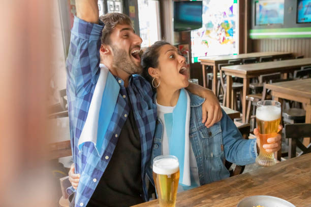 istock Couple watching soccer game on TV drinking beer in pub 1190899013