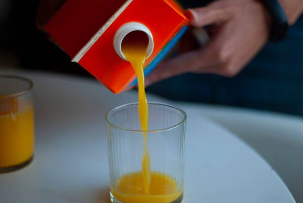Orange juice is poured into a glass Orange juice is poured into a glass from a carton of juice. juice carton stock pictures, royalty-free photos & images
