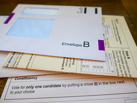 UK General Election postal vote ballot papers. The paperwork includes a return envelope, instructions on how to complete the postal vote and a ballot paper with constituency candidate names and details on how to vote for just one candidate by putting a cross in the box next to the voters choice.