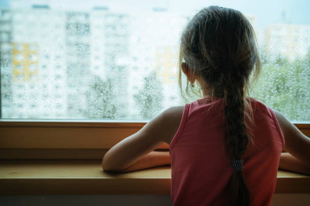 빗방울이 많은 창문 유리를 들여다보는 작은 슬픈 소녀 펜션. 슬픔과 외로움 어린 시절 개념 이미지입니다. - lot 뉴스 사진 이미지