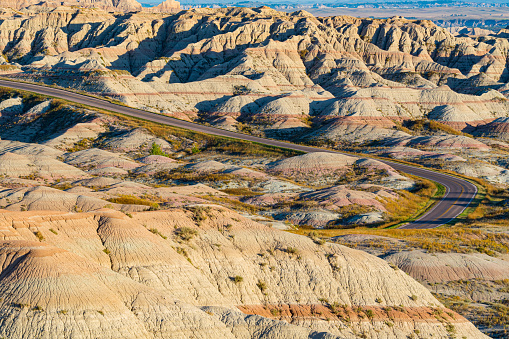 Yellow Mounds from Conata Basin Overlook, Badlands National Park, South Dakota, USA. The road with several tourist vehicles winds its way through the mounds.