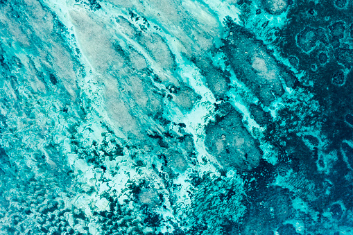 Abstract view directly taken from above and by drone of a blue tropical lagoon with coral reefs and creating blue tints of shades and lights.