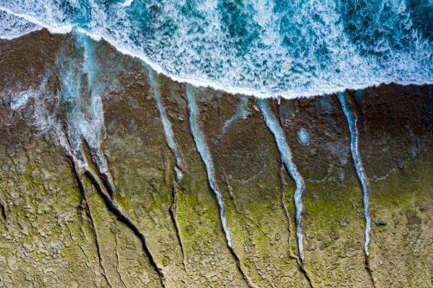 Drone view of waves breaking and dripping along a coastline