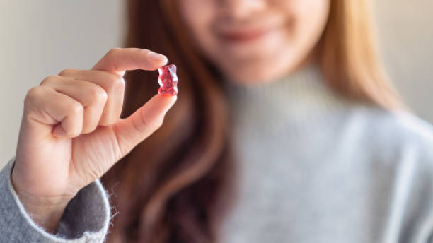 uma mulher bonita que prende e que olha um urso gummy da geléia vermelha - gummy - fotografias e filmes do acervo