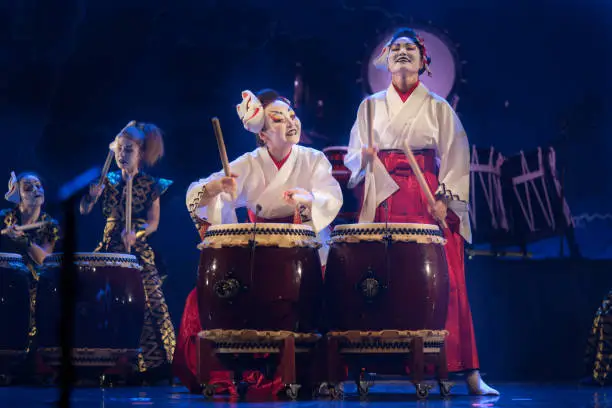 Photo of Traditional Japanese performance. Group of actresses in traditional kimono and fox masks drum taiko drums on the stage.