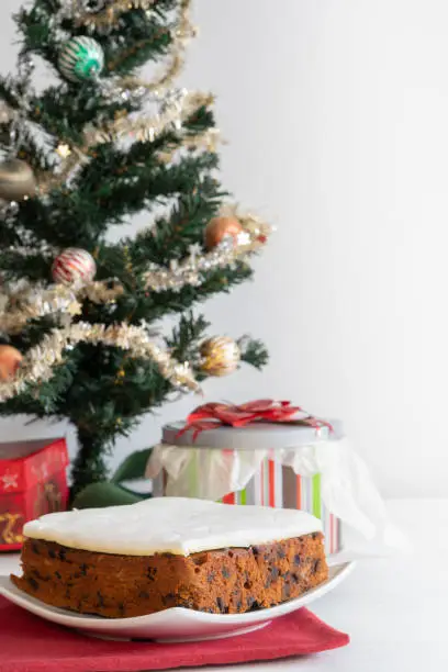 Rich Fruit Christmas Cake in front of a tree on light background with copy space Vertical