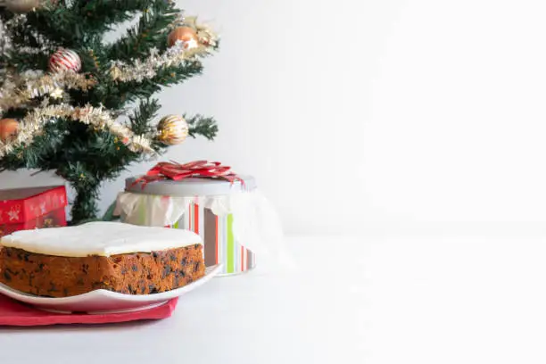 Rich Fruit Christmas Cake in front of a tree on light background with copy space horizontal