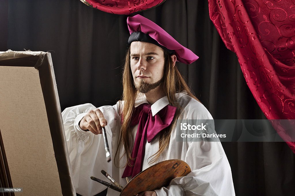 Artist at work Fine art painter wearing a renaissance clothing, holding artist pallete while painting a canvas on an easel.  Artist Stock Photo