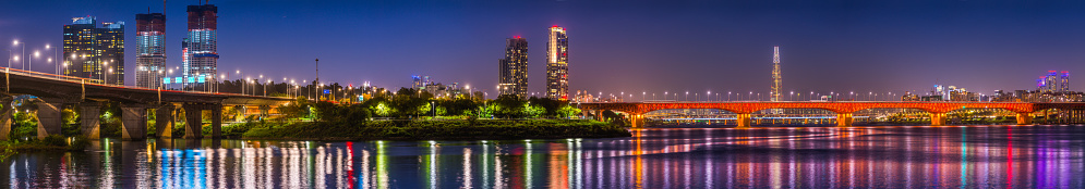 Highrise cityscape and glittering neon night skyscrapers reflecting in the tranquil waters of the Han River in the heart of Seoul, South Korea’s vibrant capital city.