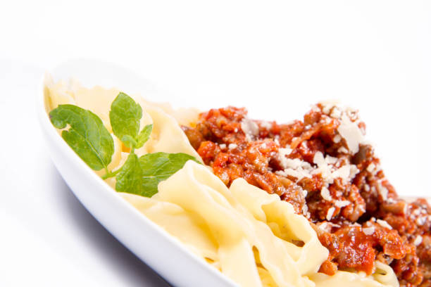 Reginette pasta with bolognese sauce decorated with parmesan and fresh herbs on a plate on a white background