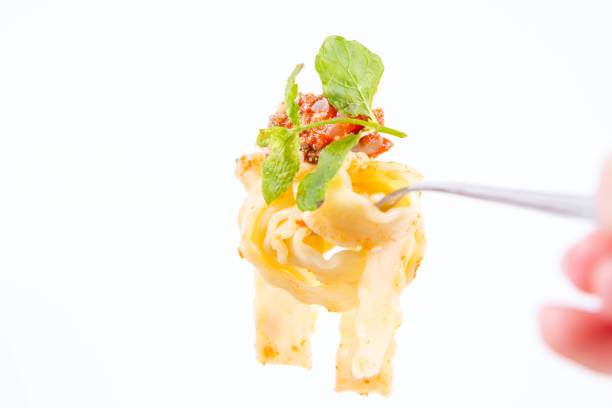 Reginette pasta with bolognese sauce decorated with parmesan and fresh herbs on a fork on a white background, held by a female hand
