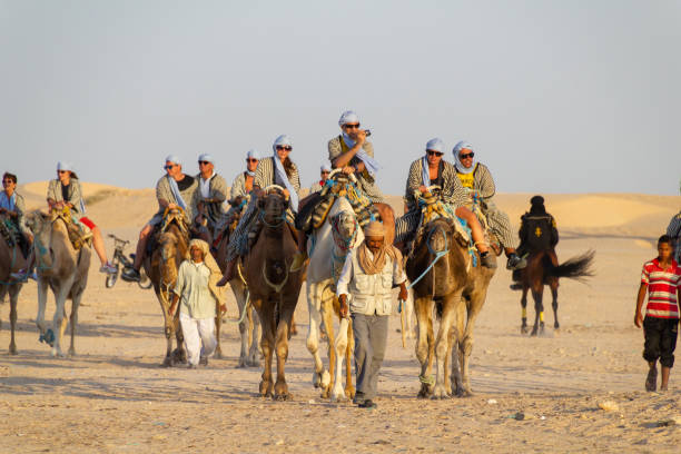 Douz, Tunisia - 8 Sept, 2014: Tourists in traditional clothes on a camel ride through the Sahara desert