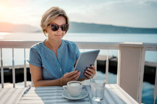 женщина, сидящая в кафе, работающая на цифровом планшете у моря - e reader digital tablet cafe reading стоковые фото и изображения