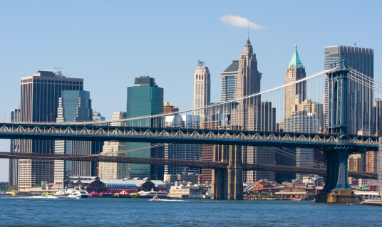 Dumbo district view in Brooklyn with Manhattan Bridge and New York City in the background. Raining day in NYC. There is a rainbow in the cloudy sky.