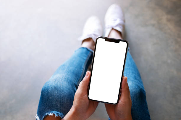 istock a woman holding black mobile phone with blank white screen while sitting on the floor 1190991786