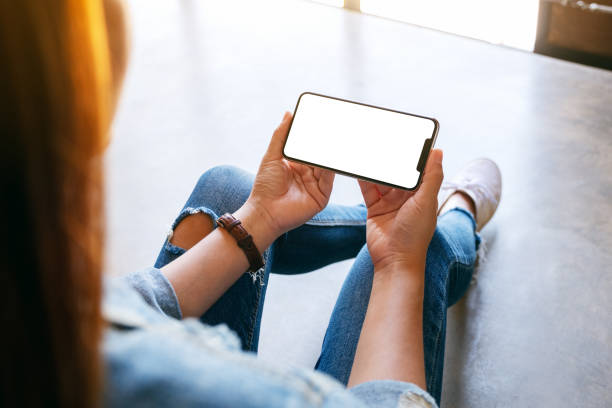 istock a woman holding black mobile phone with blank white screen while sitting on the floor 1190991797