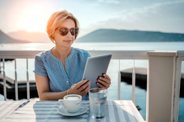 женщина, сидящая в кафе, работающая на цифровом планшете у моря - e reader digital tablet cafe reading стоковые фото и изображения